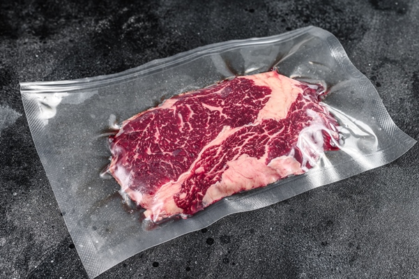 raw rib eye beef meat steak in vacuum packaging on black table top view - Правила выбора и приготовления мяса