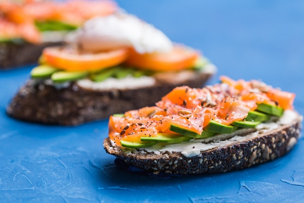 sandwiches with smoked salmon eggs sauce and avocado on blue background concept of breakfast and - Бутерброды на поджаренном хлебе