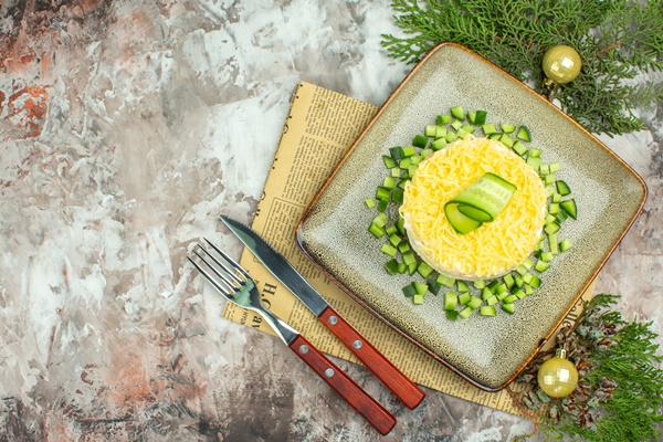 top view of tasty salad served with chopped cucumber and knife fork on an old newspaper decoration accessories on mixed color background - Правила приготовления салатов