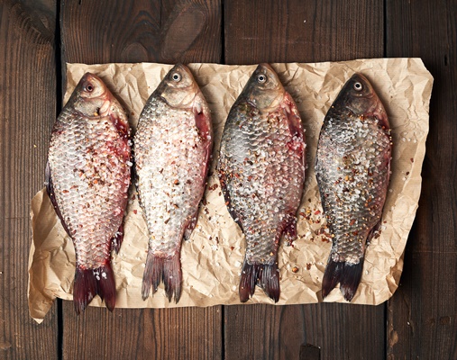 whole fresh crucian fish with scales on a crumpled brown piece of paper - Караси в сметане
