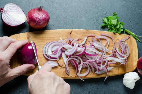 a man cuts red onions on a wooden chopping board with a kitchen knife preparing food hands close up 1 - Монастырская кухня: ржаные пирожки с горохом, постный рассольник