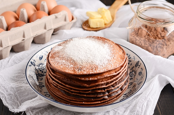 a pile of pancakes with a wooden spoon of butter eggs on a rustic wooden table - Шоколадный блинный торт