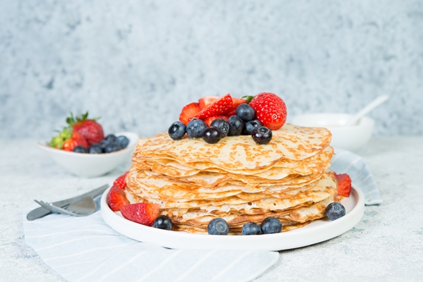 a stack of crepes lies in a plate decorated with berries on a gray concrete background top view copy of space - Блинчики с бананами (видео)