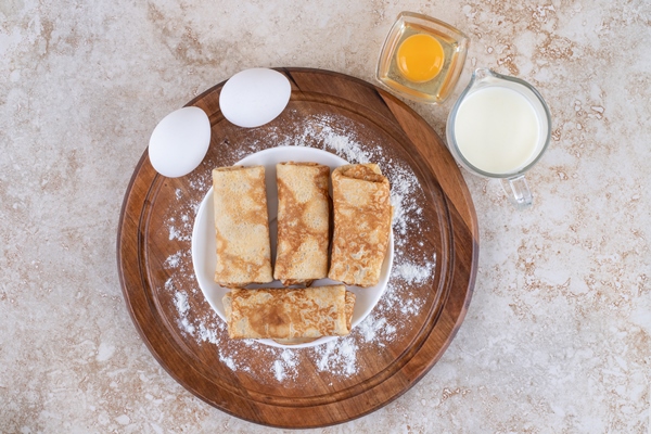 a wooden board with delicious crepes and raw eggs - Блинчики с сыром и яйцом