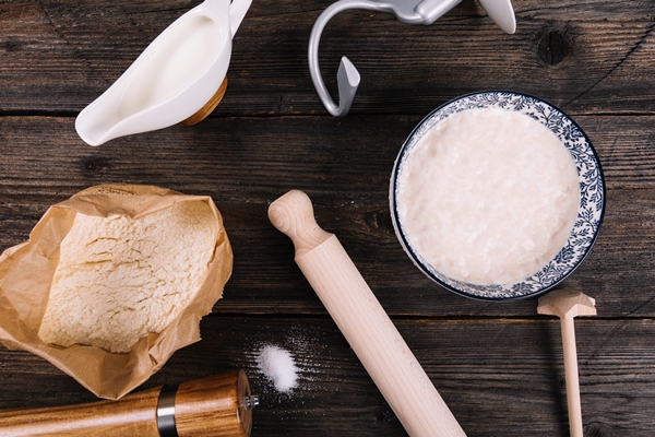 an overhead view of flour milk yeast and peppermill with rolling pin on table - Пирожки жареные дрожжевые