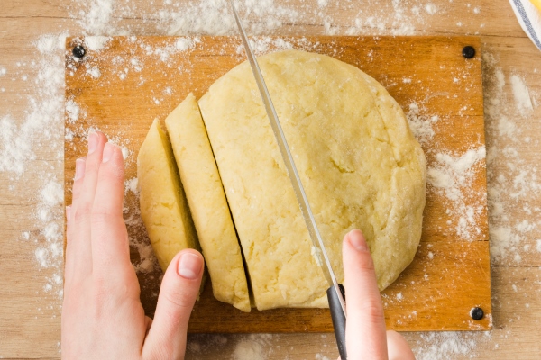 an overhead view of woman s hand cutting the dough for preparing italian gnocchi pasta on wooden table - Монастырская кухня: овощи в кляре, морковные клёцки