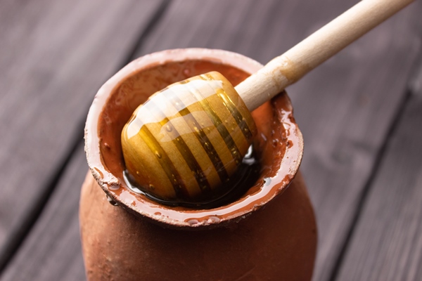 bee honey in a clay pot on a wooden table wooden spatula for honey side view close up healthy food farm apiary - Монастырская кухня: калья и ягодный десерт (видео)
