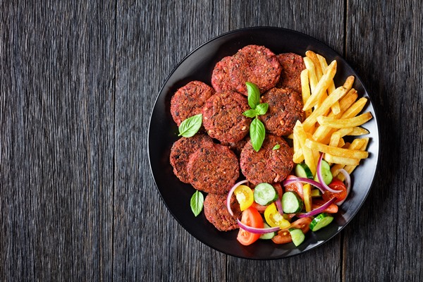 beet patties with mushrooms and black beans served with french fries and a vegetable salad of tomato cucumber red onion and fresh basil on a black plate on a dark wooden table top view free space - Монастырская кухня: луковый суп с капустой, свекольные котлеты