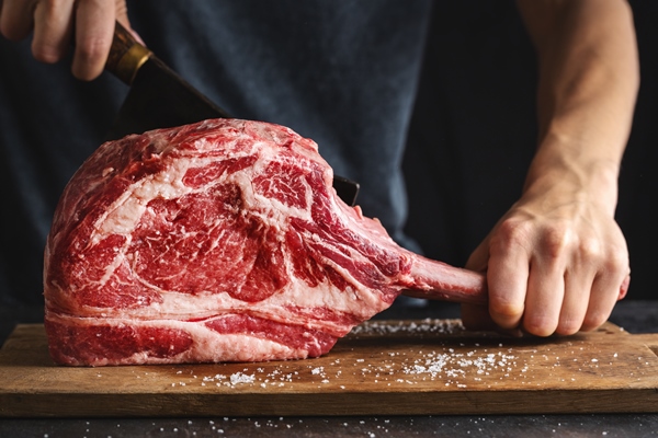 butcher cuting fresh appetizing tomahawk steak on old wooden board closeup - Телятина жареная