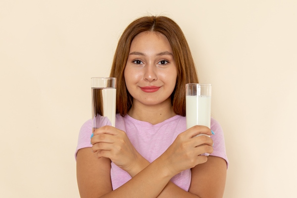 front view young attractive female in pink t shirt and blue jeans holding glasses of water and milk with smile - Налистники