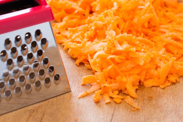 grated carrots and a small grater on the wooden table - Монастырская кухня: овощи в кляре, морковные клёцки (видео)
