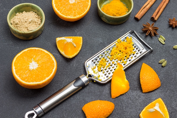 grated zest on grater slice of orange peel on grater orange halves dry ginger and turmeric spices on table black background top view - Монастырская кухня: рисовая каша с морковью, печенье макруд