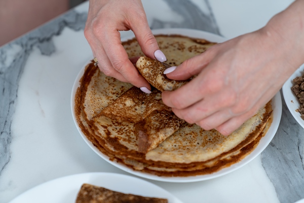 hands of the chef wrapping the filling in a pancake 1 - Блинчики с грибами, картофелем и луком