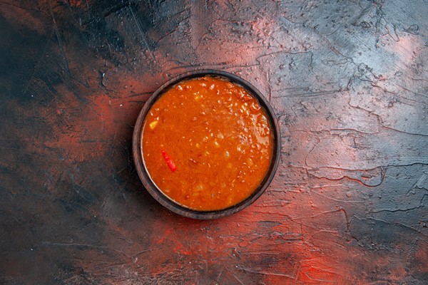 horizontal view of tomato soup in a brown bowl on mixed color table - Соус луковый острый