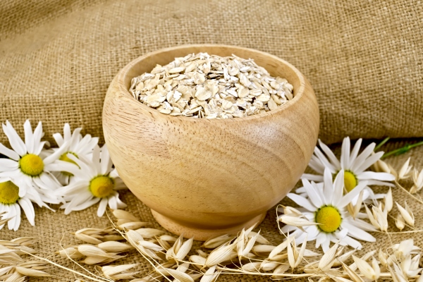 oat flakes in a wooden bowl stalks of oats chamomile on burlap and wooden board - Монастырская кухня: овсяная каша на грибном бульоне, вафли с яблоком