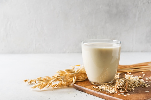 oat milk in glass with flakes and spike or ears of grain on white background - Овсянка с яблоком и корицей