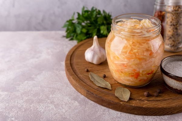 open glass jar of homemade salad sauerkraut on round cutting board close up with spicy bay leaf garlic salt parsley on gray background copy space fermented healthy food - Монастырская кухня: чечевичный суп с квашеной капустой, жареные пирожки с капустой