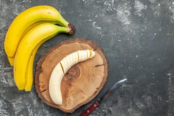 overhead view nutrition source fresh bananas bundle and chopped on wooden cutting board knife on gray background - Овсянка с манго, бананом и чиа