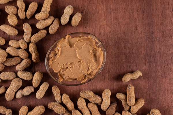 peanut butter surrounded by raw peanuts on wooden with copy space - Арахисовая паста с мёдом