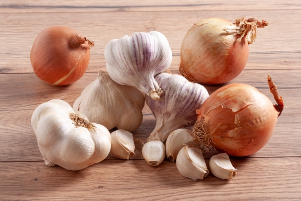 pile of whole onions and garlic bulbs and cloves on a wooden table - Помидоры, фаршированные рисом