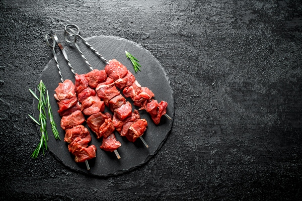raw kebab with rosemary on black wooden table - Бастурма-шашлык