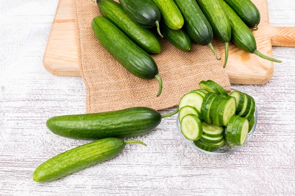 side view cucumber sliced in glass bowl on beige linen bag with cutting board on white wooden - Постный суп из овощей и водорослей