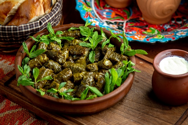 side view of traditional dolma in grape leaves with sour yogurt on a wooden table - Долма