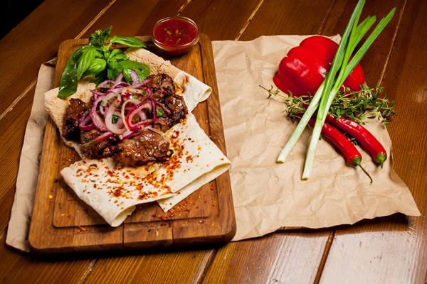 skewers of lamb with sauce with onions lavash turkish and arabic oriental traditional kebab with vegetables onions tomatoes bell peppers pita bread and lettuce on a wooden background - Шашлык по-карски