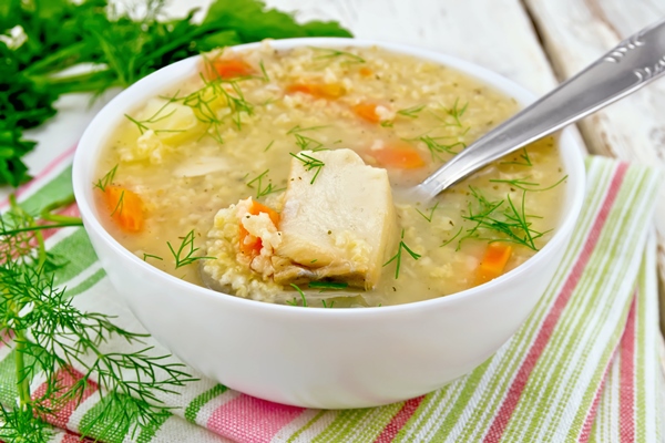 soup fish kulesh with millet potatoes and carrots and spoon in a bowl on a napkin parsley dill on a wooden board background - Монастырский кулеш