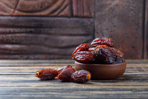 sweet dates in a clay plate on stone tile and wooden background - Монастырская кухня: рисовая каша с морковью, печенье макруд