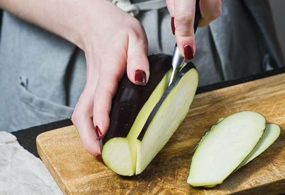 the hands of the chef slice the eggplant on wooden cutting board - Монастырская кухня: рис с баклажанами, ревани