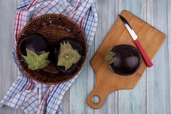 top view of eggplants with knife on cutting board and in basket on plaid cloth on wooden background 1 - Бабагануш из баклажан