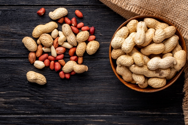 top view unshelled peanuts in a bowl with peeled on a black wooden table - Шоколадно-арахисовая паста