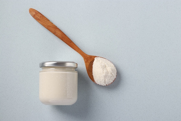 vegan organic paste of coconut in glass jar as well as coconut flour in a wooden spoon on a light blue background healthy food urbech view from above - Кокосовый урбеч