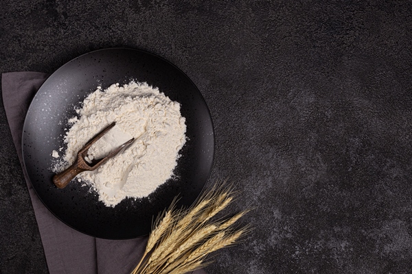 white wheat flour in a wooden spoon on a dark structural background on a plate made of black stone - Монастырская кухня: тёплый салат из баклажанов, постные корзиночки (видео)