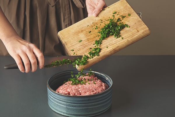 woman hands add fresh green parsley to minced meat in beautiful ceramic bowl on old wooden table - Пирожки жареные дрожжевые