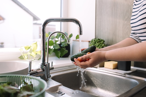 woman washing green cucumbers for salad in kitchen in sink under running water - Постная "окрошка" с водорослями