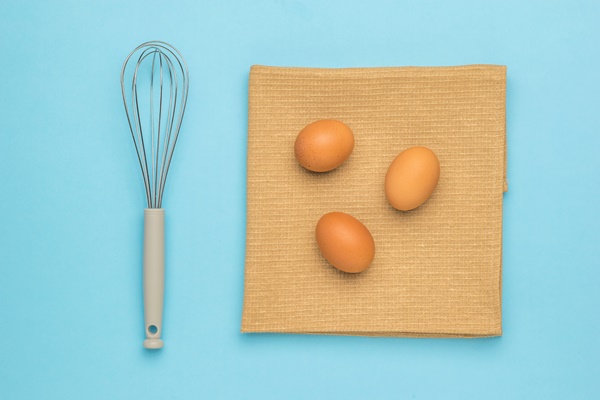 a whisk for whipping and three eggs on a piece of cloth on a blue surface natural products and kitchen equipment - Пасхальная мона
