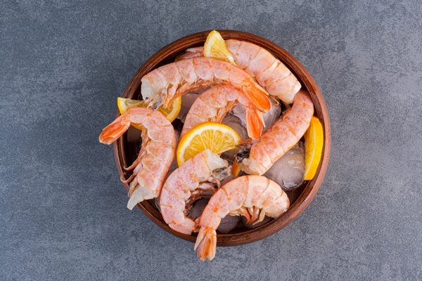 a wooden plate of delicious shrimps with ice cubes and sliced lemon on a stone surface - Постный салат с кальмарами, икрой и креветками