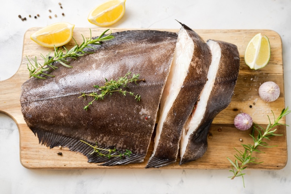 close up of fresh raw halibut fish on wodden board with herbs and lemon top view omega 3 fats good for mental clarity brain food - Камбала или палтус, запечённые в духовке
