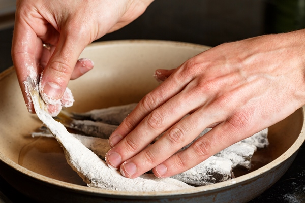 closeup of man hands put the fresh fish smelt in flour on frying pan unhealthy food on oil - Жареная корюшка