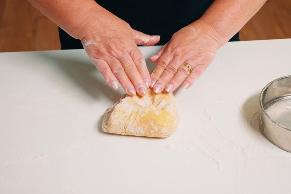 closeup shot of hands of senior bakery kneading dough retired elderly baker with bonete mixing ingredients with sifted wheat flour forming on a floured surface for baking traditional cake bread - Постные луковые лепёшки