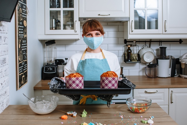 cook woman in a medical mask holding a baking tray with easter cakes - Куличи александрийские