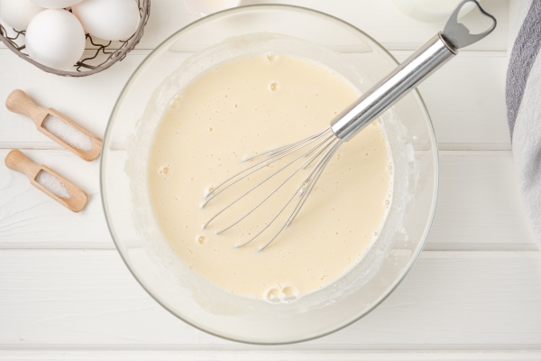 cooking dough for traditional thin pancakes or crepes eggs flour salt sugar milk and butter in a bowl on a white wooden background - Царская пасха без творога с лимонным соком