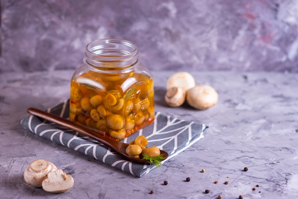 fermented canned champignon mushrooms in a wooden eco spoon and in a glass jar with garlic bay leaf on a gray napkin with dill - Лечебный стол (диета) № 3 по Певзнеру: таблица продуктов и режим питания