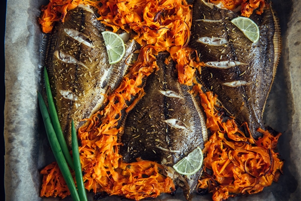 fish baked on baking sheet with vegetables close up flounder on parchment with carrots lime and green onions - Камбала с овощами