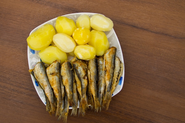 fried baltic herring with boiled potatoes on a plate on wooden background - Салака в крахмальной панировке