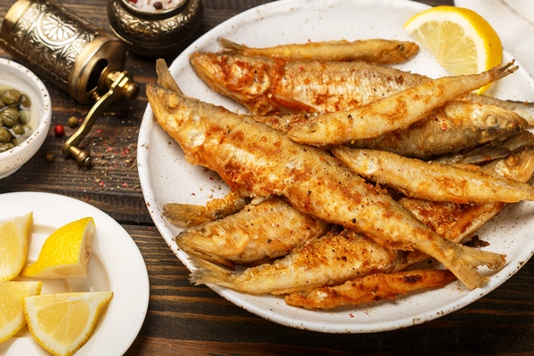 fried smelt in a white plate small fish capers lemon pepper and salt on a wooden table a delicious dinner in the rustic style - Корюшка по-ленинградски