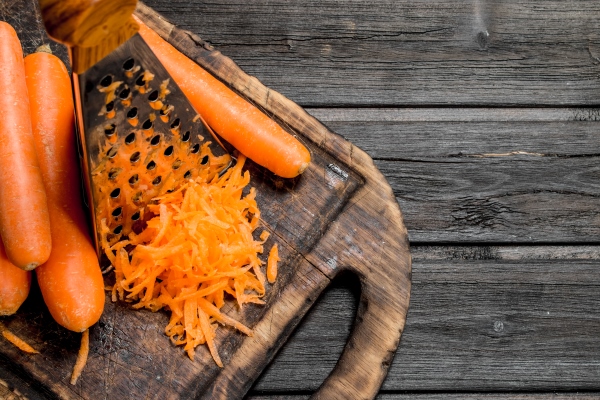 grated carrots on a cutting board with a grater on wooden background - Цукини, фаршированные кашей и баклажанами