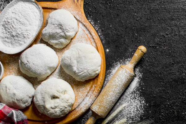pieces of dough with flour eggs and a napkin on black rustic table - Постные лепёшки с зеленью (кутабы)